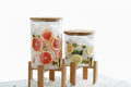 Two glass containers with fruit infusions on stands in a bright room.